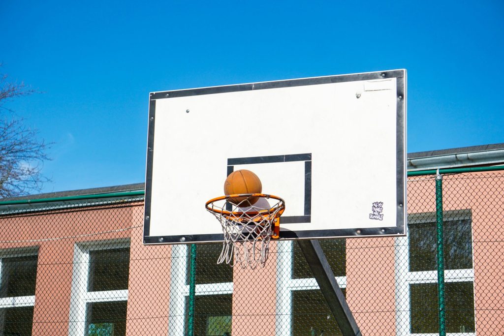 Una pelota de baloncesto reposa en un aro contra un cielo azul claro en una cancha al aire libre.